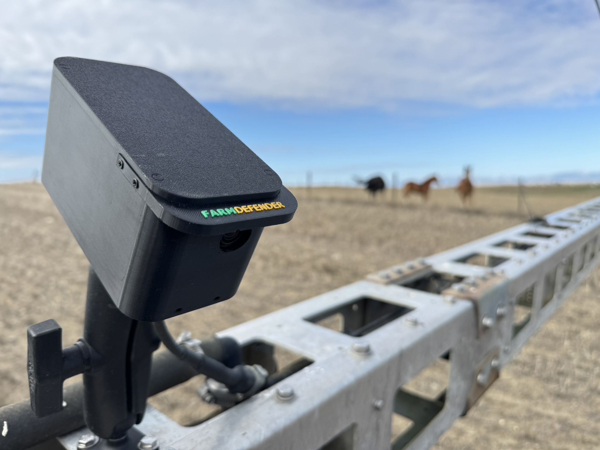 FarmDefender camera unit mounted on a sprayer boom — close-up showing the hardware, Montana field background